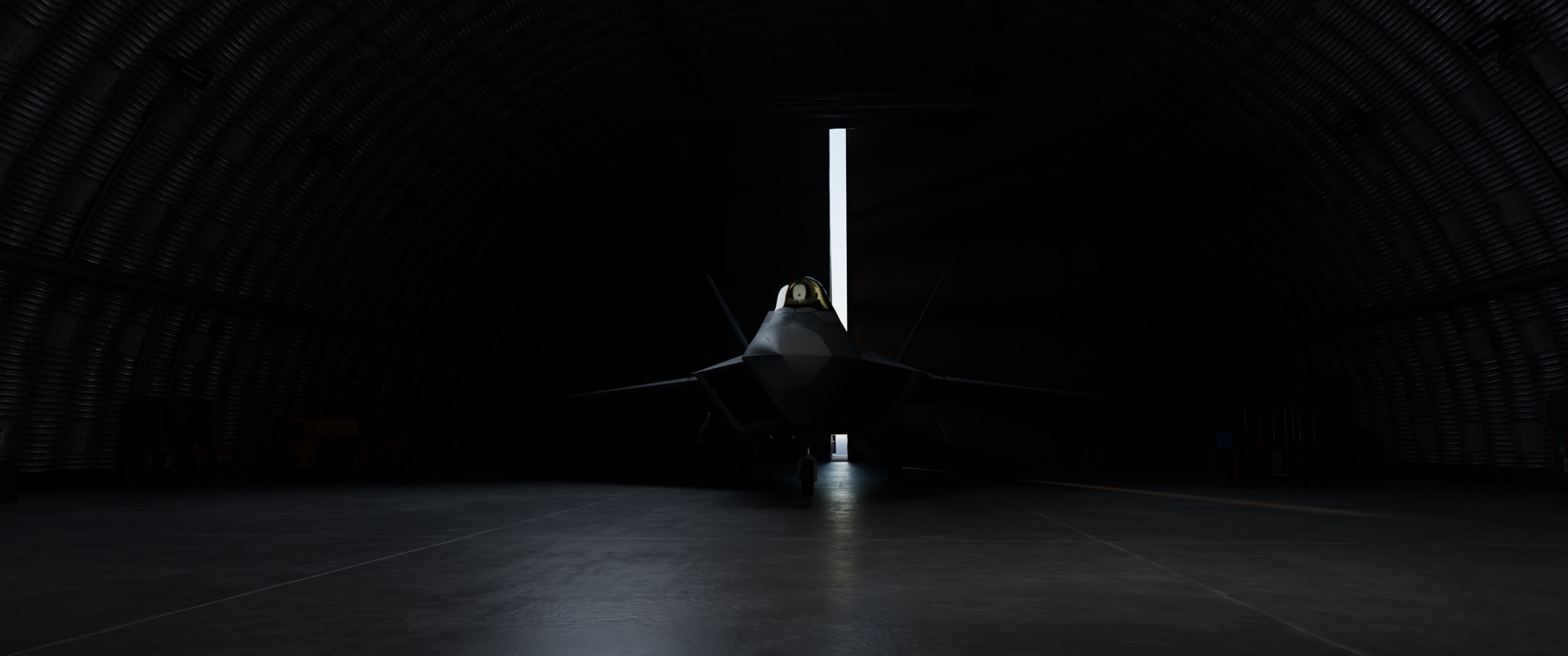 An F-22 nose-on in a dark hangar, a strip of daylight behind it